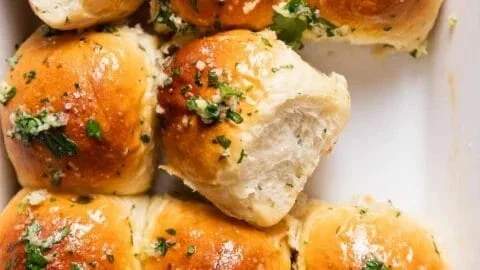 Freshly baked garlic bread rolls with herbs and cheese on a wooden table